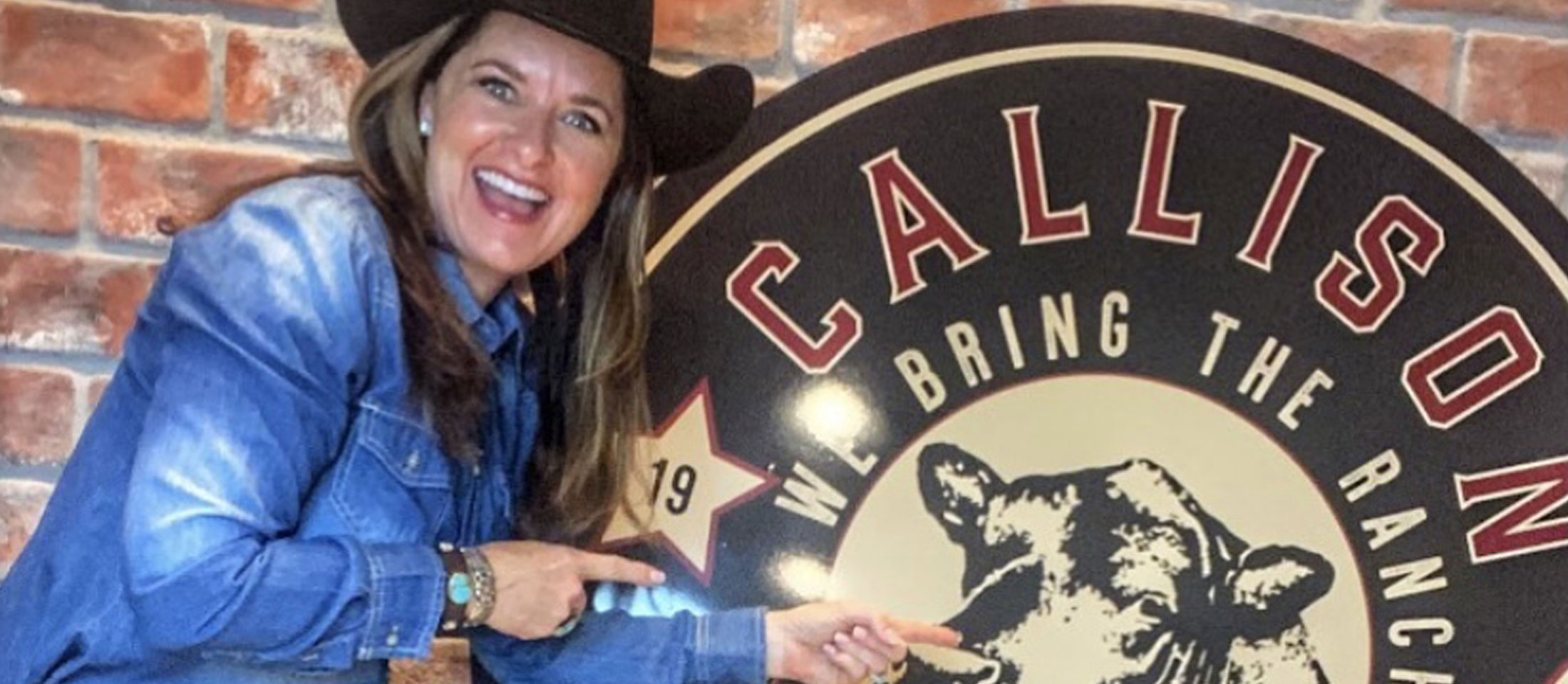 A cowgirl wearing a black cowboy hat posing with a circular sign that reads “Callison Ranch Beef”.